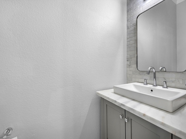 bathroom with decorative backsplash, vanity, and a textured wall