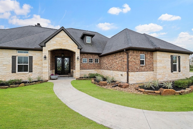 french country inspired facade featuring french doors, stone siding, a front lawn, and a shingled roof