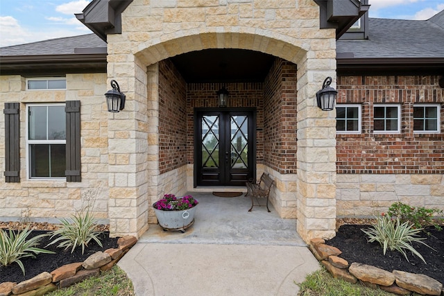 doorway to property featuring brick siding, french doors, stone siding, and a shingled roof