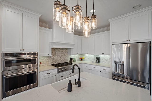 kitchen with a sink, white cabinets, appliances with stainless steel finishes, a notable chandelier, and backsplash