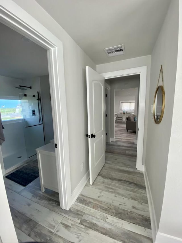 hallway featuring plenty of natural light, wood finished floors, visible vents, and baseboards