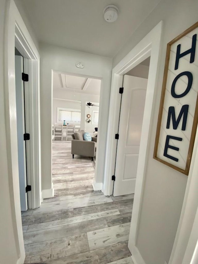 hall with baseboards, attic access, and wood finished floors