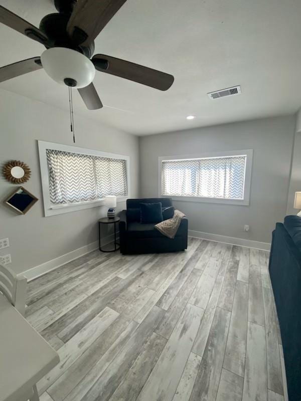 living area with visible vents, baseboards, a ceiling fan, and wood finished floors