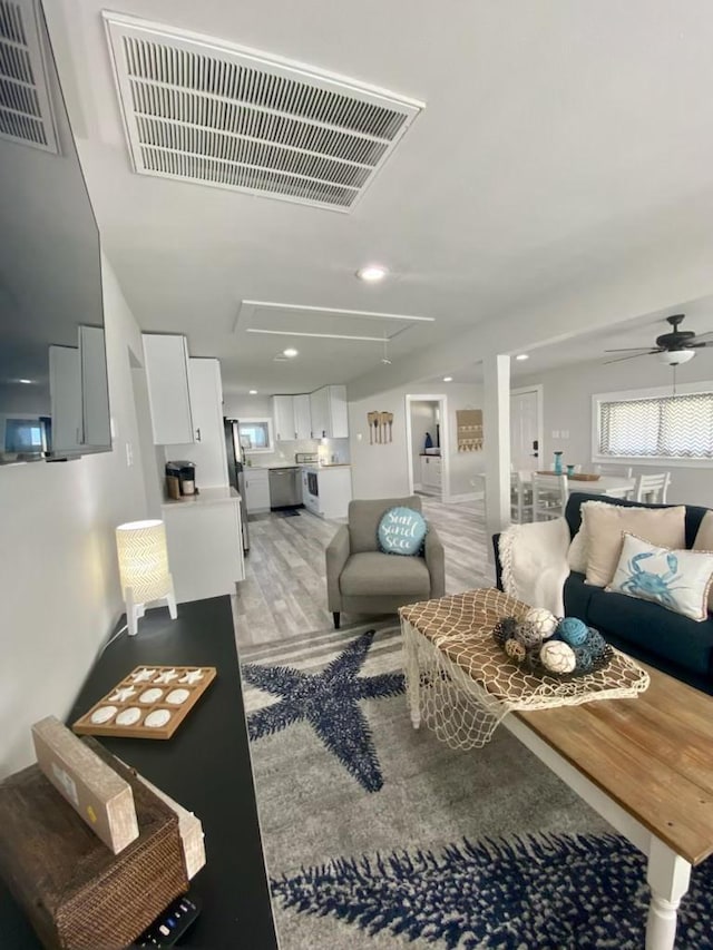 living area featuring visible vents, light wood-style flooring, attic access, and ceiling fan