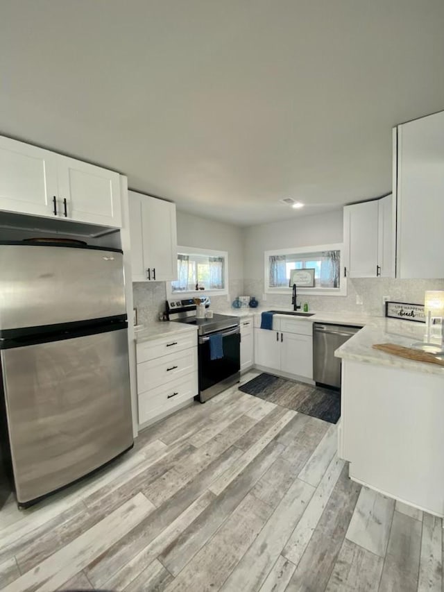 kitchen with light wood-style flooring, a sink, backsplash, stainless steel appliances, and white cabinets