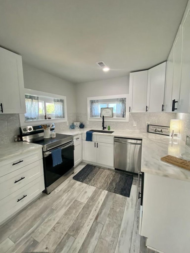 kitchen featuring white cabinets, backsplash, appliances with stainless steel finishes, and a sink