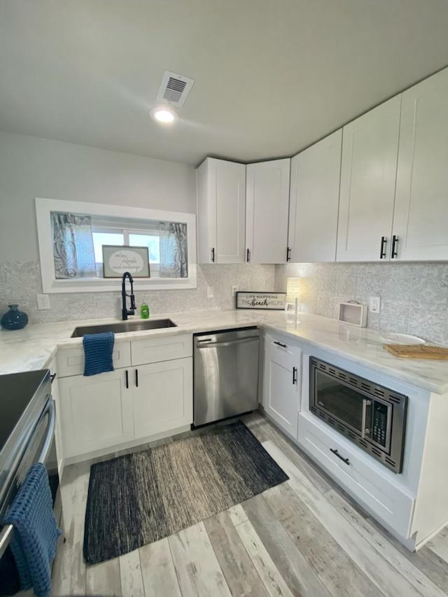 kitchen with tasteful backsplash, visible vents, appliances with stainless steel finishes, white cabinets, and a sink