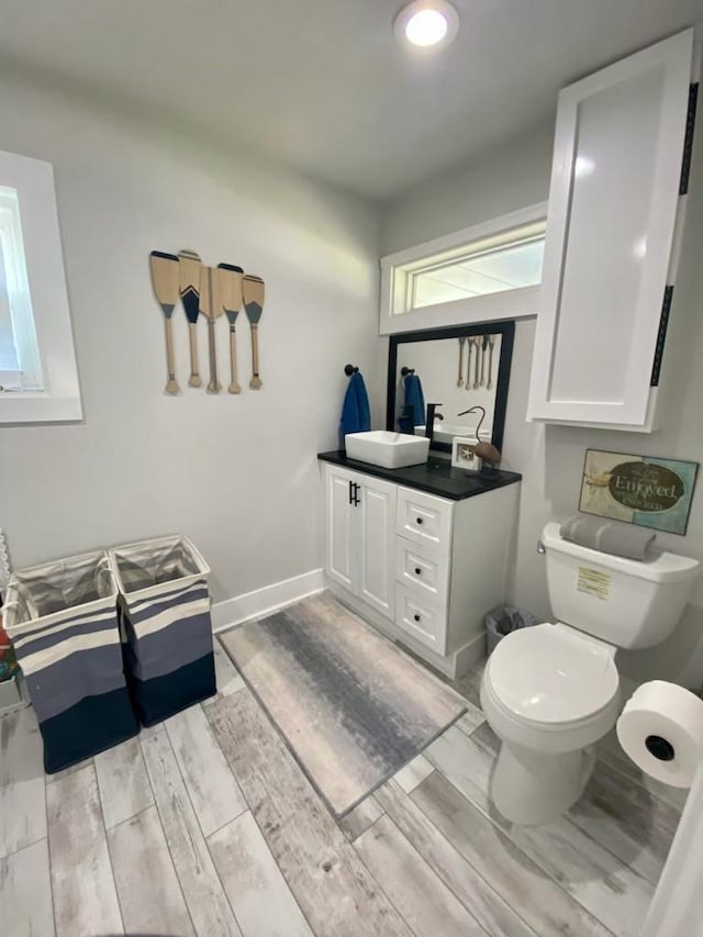 bathroom with vanity, toilet, wood finished floors, and baseboards