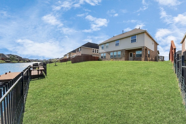 back of house with brick siding, a lawn, fence, and a water view