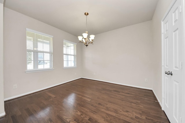 unfurnished room with a chandelier, dark wood finished floors, and baseboards