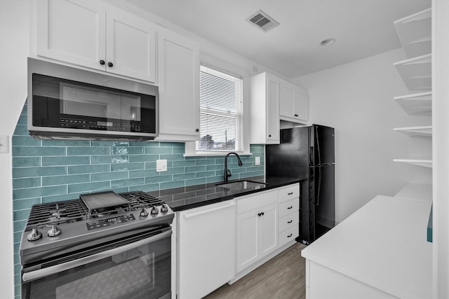 kitchen featuring visible vents, backsplash, white cabinets, stainless steel appliances, and a sink