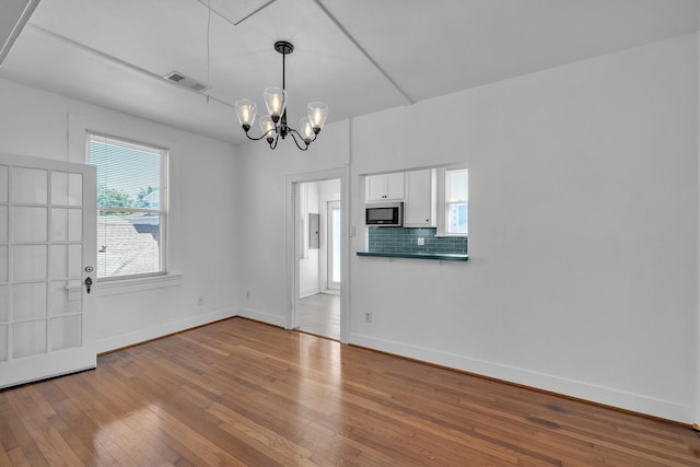 interior space featuring baseboards, visible vents, wood-type flooring, and a chandelier