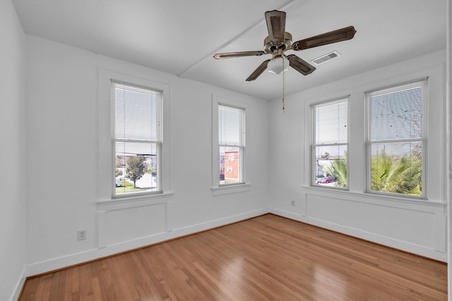 spare room featuring a wealth of natural light, visible vents, wood finished floors, and a ceiling fan
