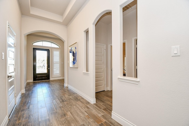 foyer featuring arched walkways, a towering ceiling, baseboards, and dark wood-style flooring