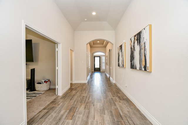 corridor with wood finished floors, arched walkways, and baseboards