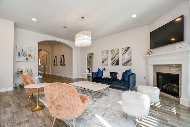 living room featuring a notable chandelier, wood finished floors, arched walkways, baseboards, and a tile fireplace