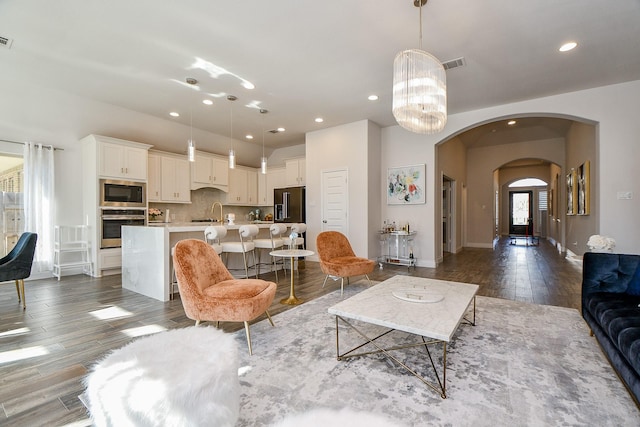 living area featuring visible vents, recessed lighting, arched walkways, dark wood-type flooring, and a chandelier