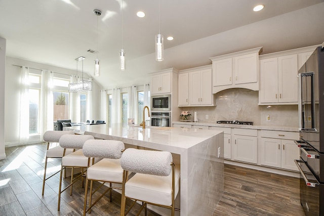 kitchen featuring stainless steel appliances, a center island with sink, decorative backsplash, and white cabinets