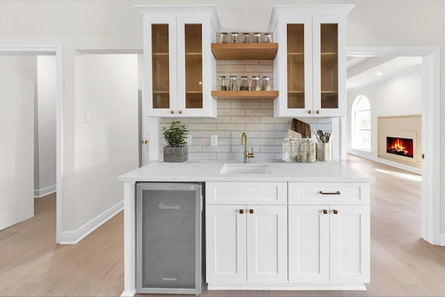 bar featuring light wood-type flooring, decorative backsplash, a warm lit fireplace, wet bar, and a sink