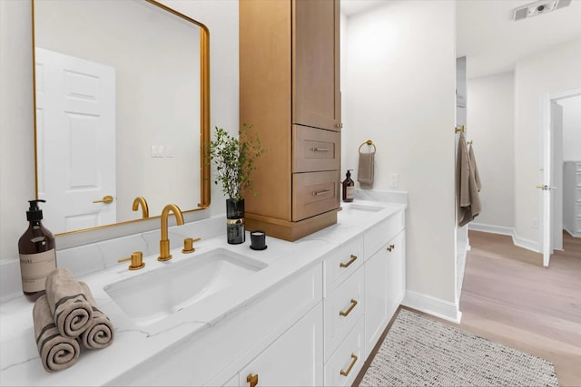 full bath with visible vents, a sink, wood finished floors, double vanity, and baseboards