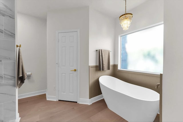 full bath with a notable chandelier, baseboards, a soaking tub, and wood finished floors