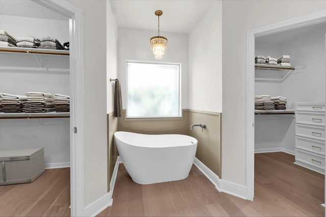 full bathroom featuring a freestanding bath, a walk in closet, and wood finished floors