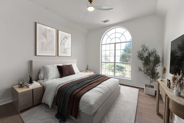 bedroom with light wood finished floors, visible vents, ceiling fan, baseboards, and a textured ceiling