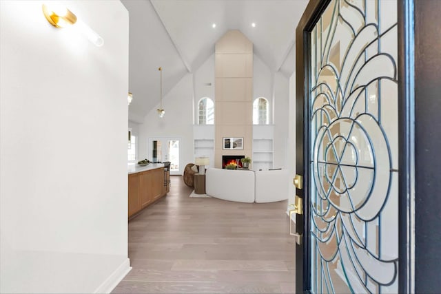 entrance foyer with a tiled fireplace, light wood-style floors, and high vaulted ceiling