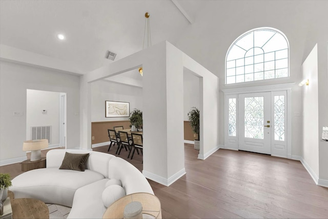 foyer entrance with a high ceiling, wood finished floors, visible vents, and baseboards