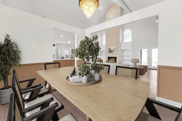 dining area with built in shelves, light wood-type flooring, wainscoting, a notable chandelier, and high vaulted ceiling