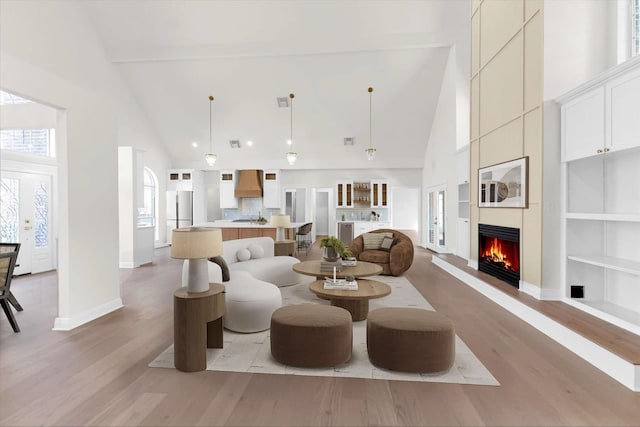 living room with built in shelves, baseboards, light wood finished floors, high vaulted ceiling, and a fireplace