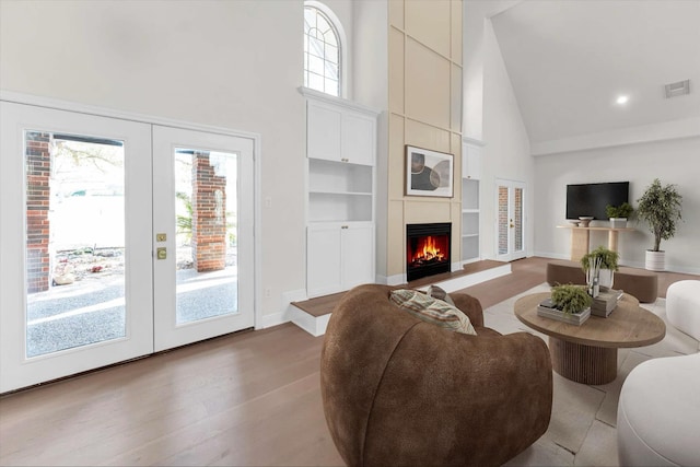 living area featuring visible vents, high vaulted ceiling, a warm lit fireplace, wood finished floors, and baseboards