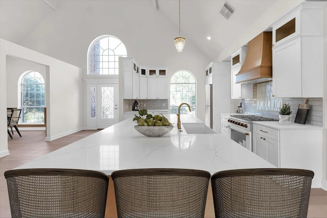 kitchen featuring white appliances, visible vents, premium range hood, high vaulted ceiling, and a sink