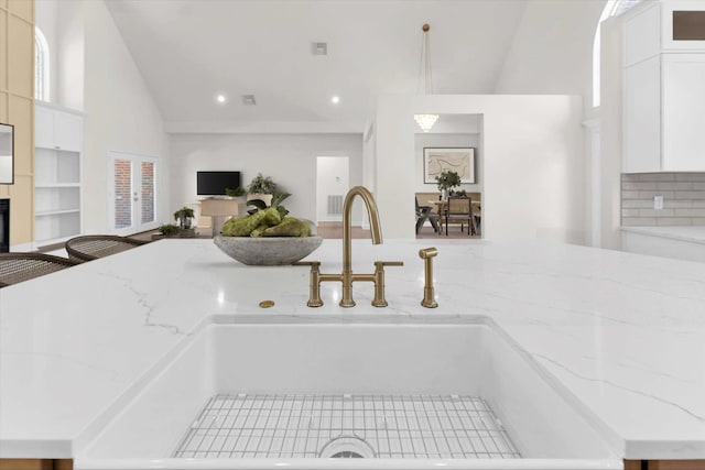 interior space featuring light stone counters, high vaulted ceiling, white cabinetry, and open floor plan