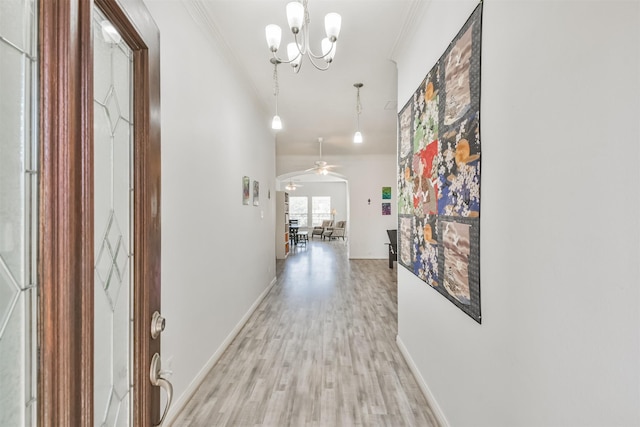 corridor with crown molding, light wood-style floors, arched walkways, and a chandelier