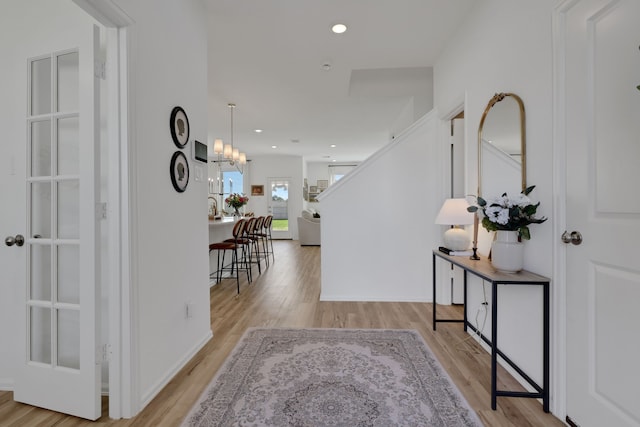 corridor with recessed lighting, stairway, an inviting chandelier, and wood finished floors