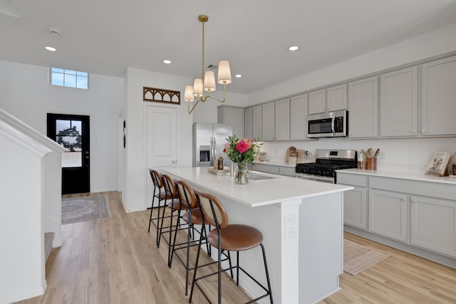 kitchen with gray cabinetry, a center island, a breakfast bar, light wood-type flooring, and appliances with stainless steel finishes