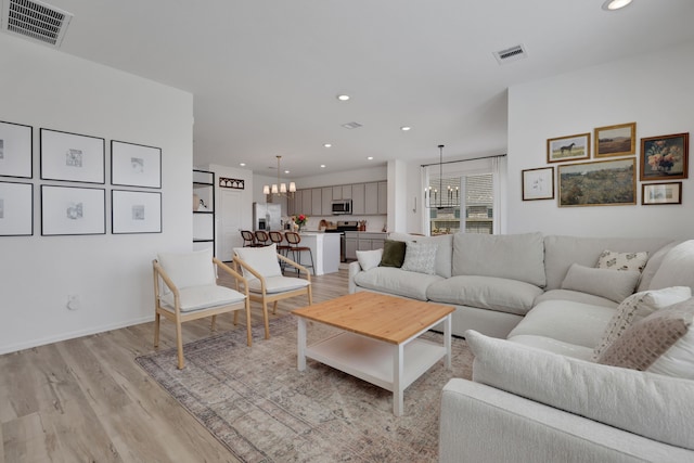 living area with recessed lighting, visible vents, light wood-style floors, and an inviting chandelier