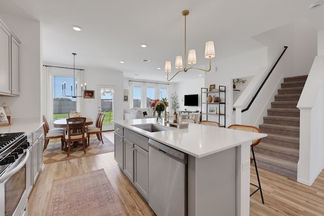 kitchen featuring an inviting chandelier, gray cabinets, a sink, stainless steel appliances, and light wood-type flooring