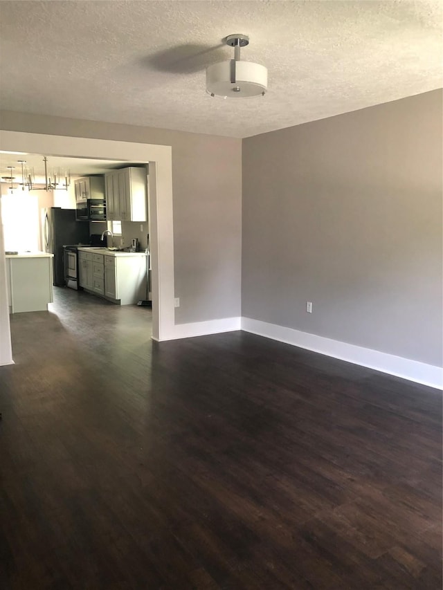 unfurnished living room with a textured ceiling, baseboards, and dark wood-style flooring