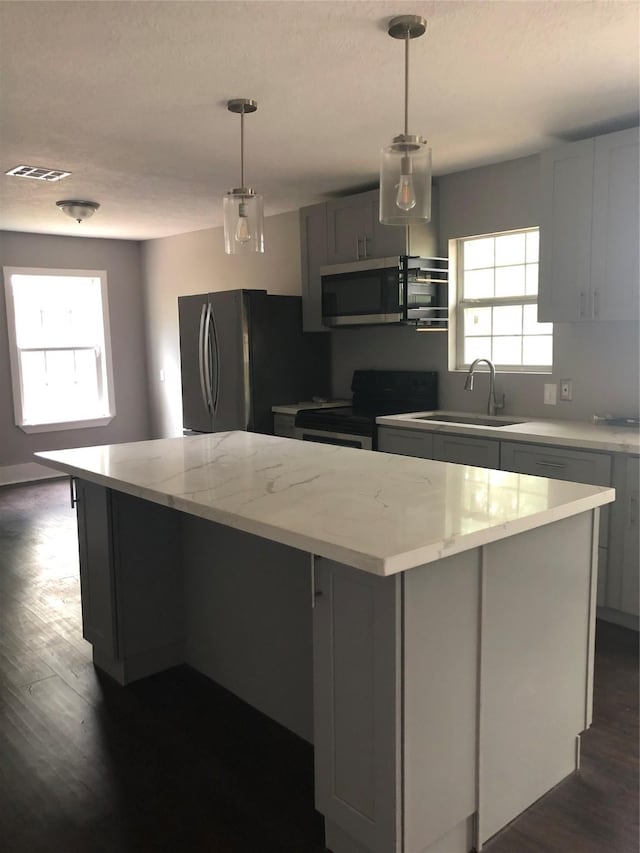 kitchen with visible vents, a sink, a kitchen island, dark wood-style floors, and appliances with stainless steel finishes