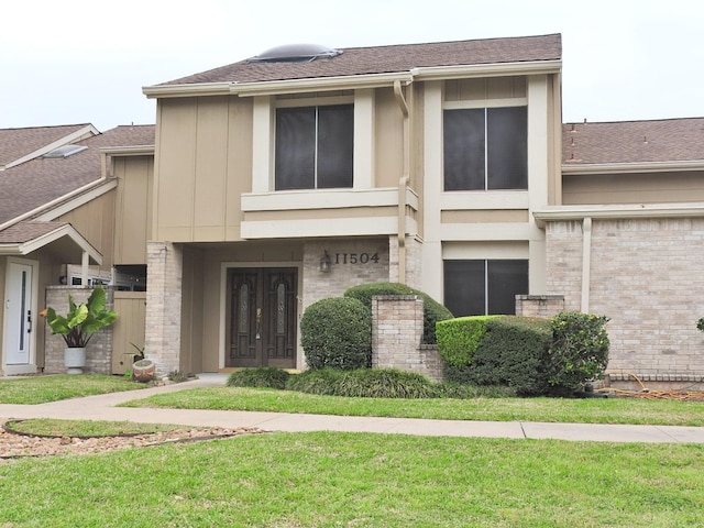 townhome / multi-family property featuring brick siding, a front yard, and a shingled roof