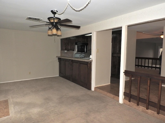 kitchen with dark brown cabinets, black microwave, ceiling fan, light countertops, and light carpet