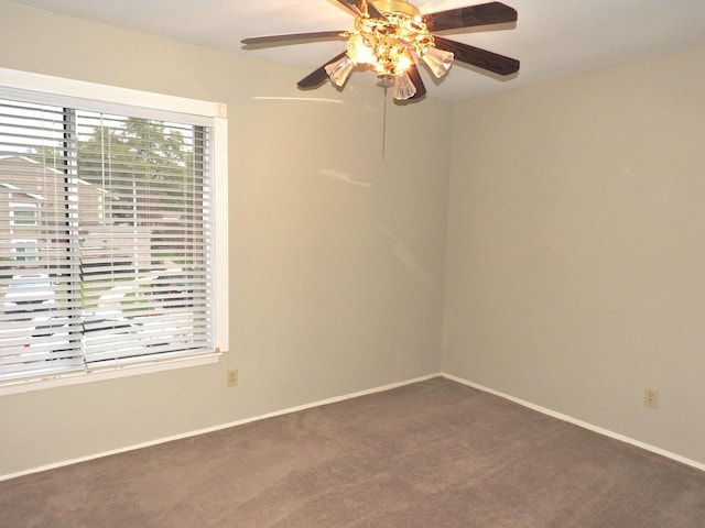 spare room featuring baseboards, dark carpet, and ceiling fan