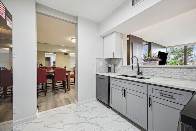 kitchen featuring marble finish floor, gray cabinets, a sink, tasteful backsplash, and dishwashing machine