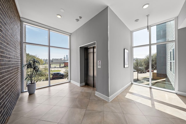 unfurnished room with baseboards, brick wall, tile patterned flooring, a towering ceiling, and expansive windows