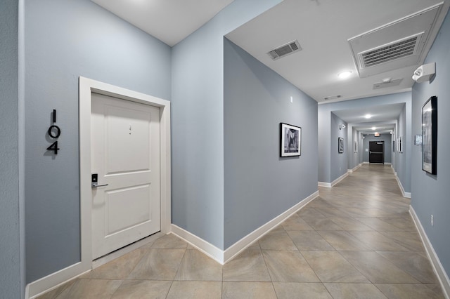 hallway with light tile patterned floors, visible vents, and baseboards