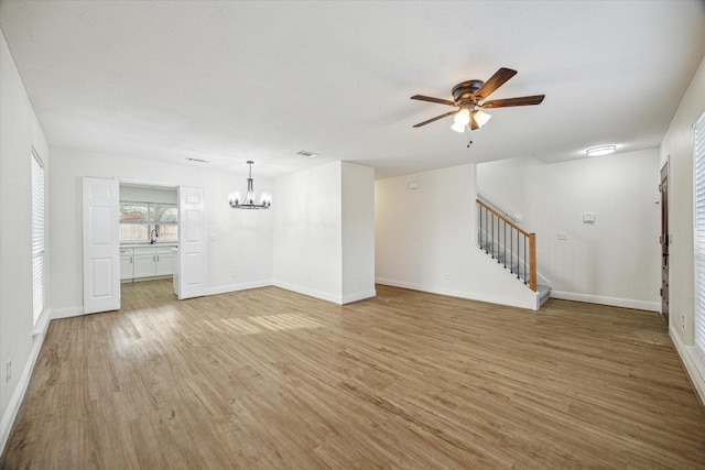 unfurnished living room featuring visible vents, ceiling fan with notable chandelier, light wood finished floors, baseboards, and stairs