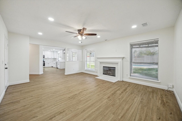 unfurnished living room featuring light wood-type flooring, visible vents, a fireplace with flush hearth, and ceiling fan