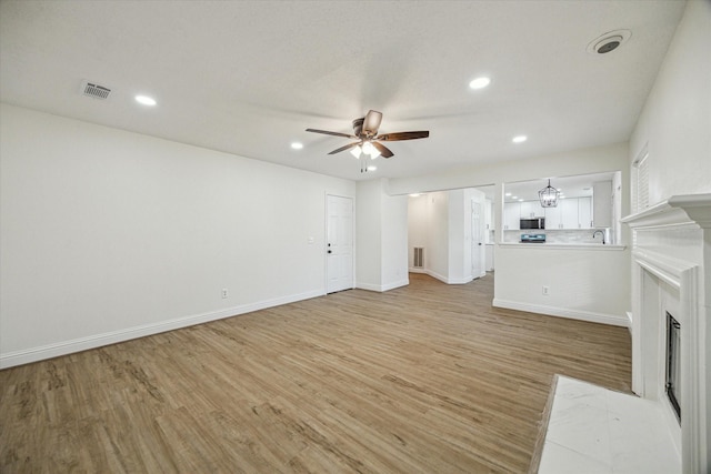 unfurnished living room with light wood-type flooring, visible vents, a fireplace with flush hearth, and a ceiling fan